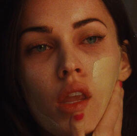 close up of jennifer check rubbing foundation onto her face with a tired, vacant expression